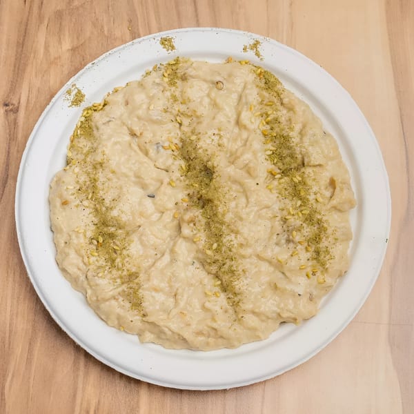 Creamy hummus or dip, garnished with green herbs and sesame seeds, on a white plate.
