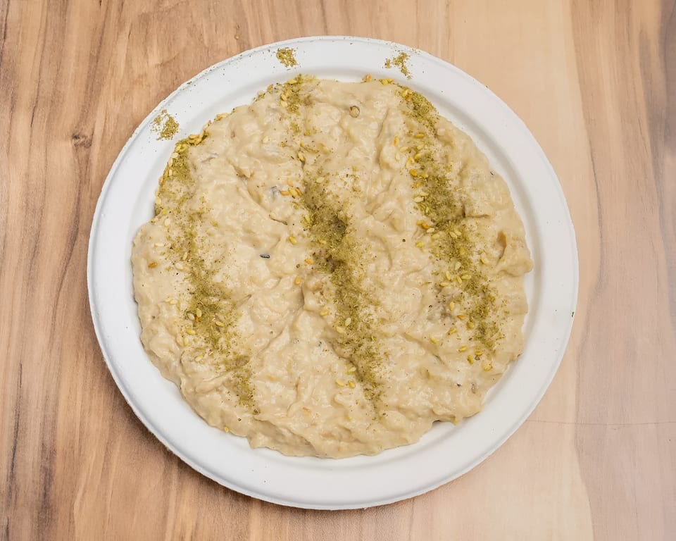 Creamy hummus or dip, garnished with green herbs and sesame seeds, on a white plate.