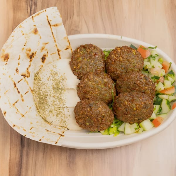A white bowl filled with falafel, hummus, pita bread, and a cucumber and tomato salad.