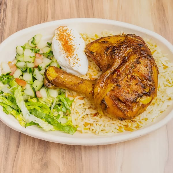 Roasted chicken leg and thigh with rice, a side salad, and a dollop of white sauce.