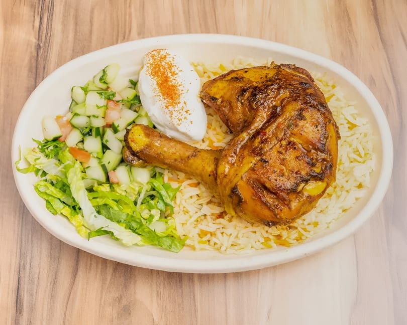 Roasted chicken leg and thigh with rice, a side salad, and a dollop of white sauce.