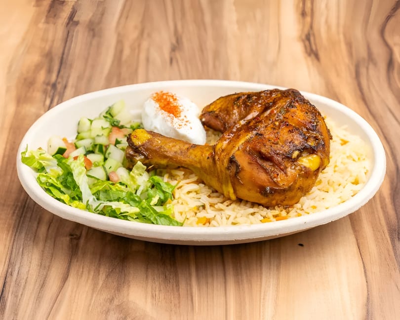 Two roasted chicken drumsticks with rice, a side salad, and a dollop of sour cream.