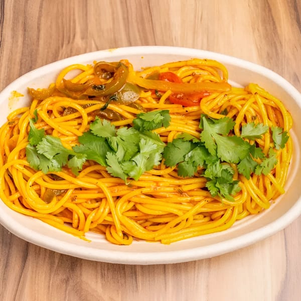 A white oval bowl filled with yellow spaghetti, bell peppers, and fresh cilantro on a wooden table.