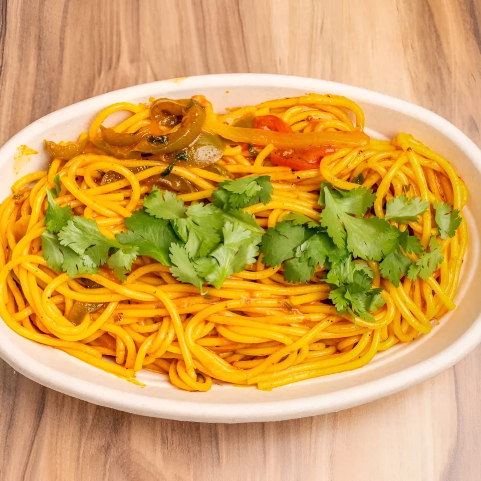 A white oval bowl filled with yellow spaghetti, bell peppers, and fresh cilantro on a wooden table.