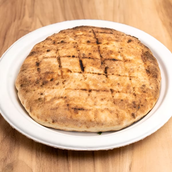 Grilled flatbread with char marks on a white plate, on a light wooden table.