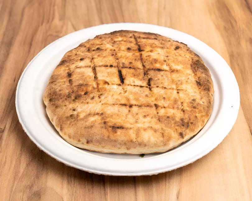 Grilled flatbread with char marks on a white plate, on a light wooden table.