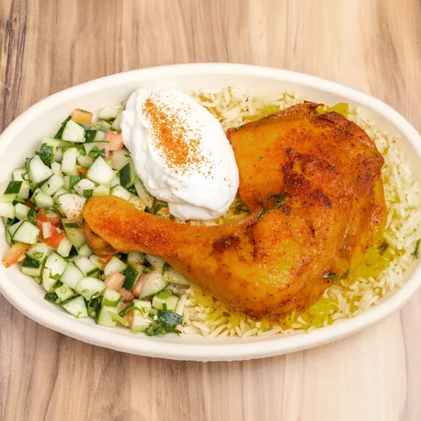 A chicken leg with rice, cucumber salad, and a dollop of sour cream in a white bowl.