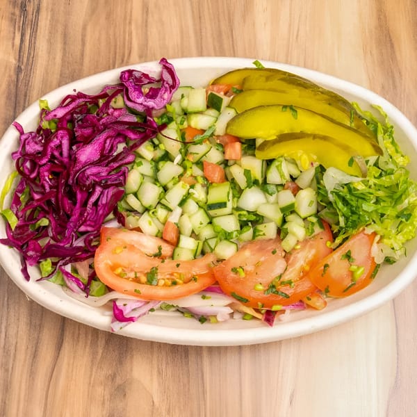 A vibrant salad with shredded red cabbage, diced cucumbers, sliced tomatoes, lettuce, and pickles.
