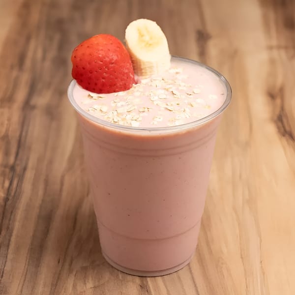 Strawberry banana smoothie in a clear cup, topped with oats, a strawberry, and a banana slice.