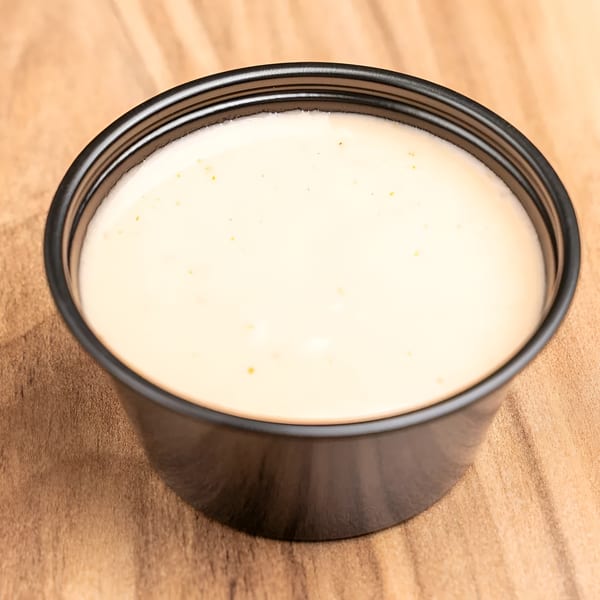 Creamy white sauce with small orange specks in a black plastic cup on a wooden surface.