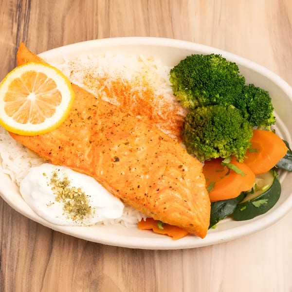 Salmon fillet with rice, broccoli, carrots, zucchini, a lemon slice, and a dollop of sauce.