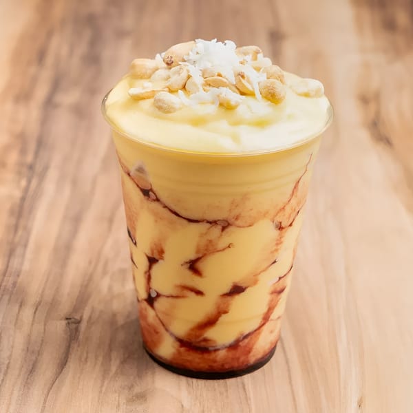 A yellow smoothie with red swirls, topped with peanuts and shredded coconut, on a wooden table.