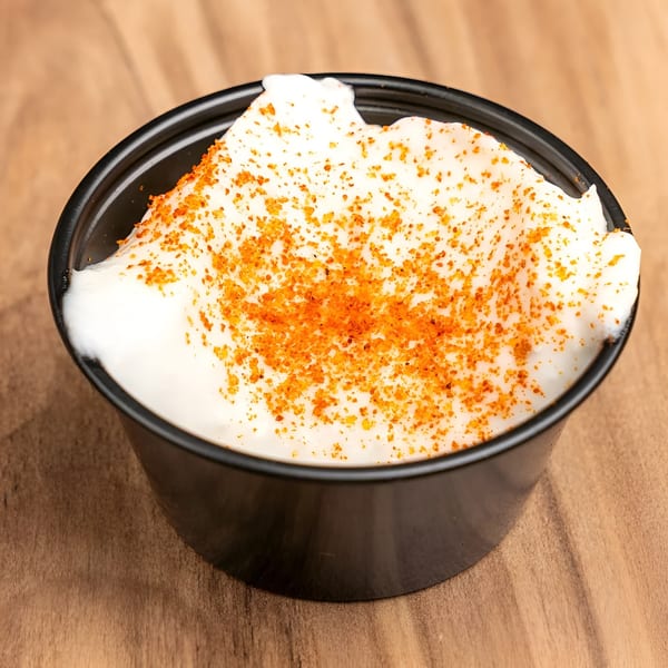 A small black cup filled with white sour cream, topped with orange seasoning, on a wooden surface.