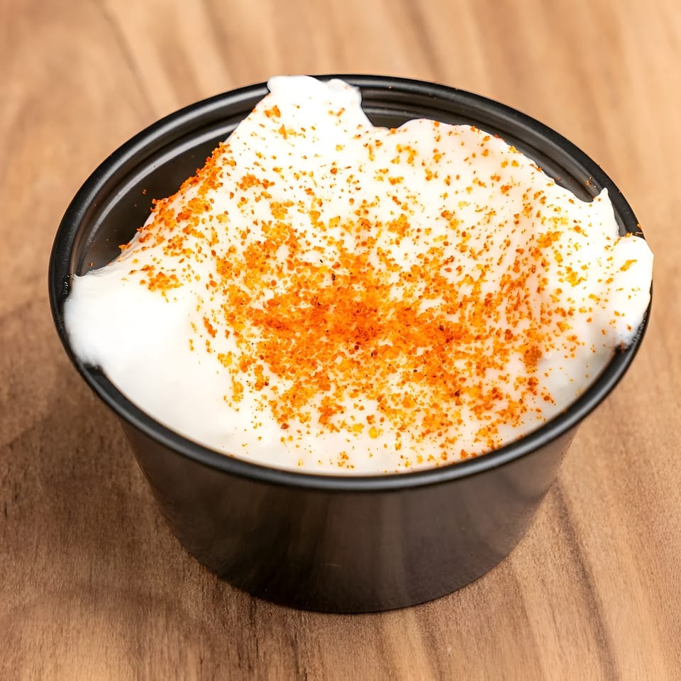 A small black cup filled with white sour cream, topped with orange seasoning, on a wooden surface.