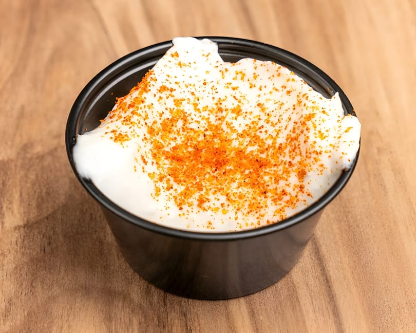 A small black cup filled with white sour cream, topped with orange seasoning, on a wooden surface.